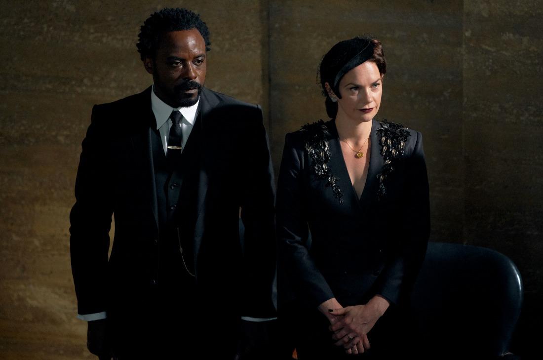 A imagem mostra Carlo Boreal, personagem de His Dark Materials, e Marisa Coulter. Carlo veste um terno preto, e Marisa um vestido preto com acessório na cabeça.
