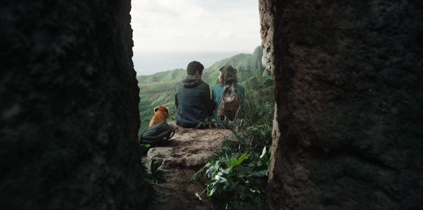 Pan, em forma de panda vermelha, Will e Lyra estão sentados na beirada de um penhasco. Ao fundo, pode-se ver uma floresta. A câmera se posiciona atrás deles, mostrando as costas. 