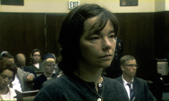 Cena do filme Dançando no Escuro. A imagem mostra Björk em um tribunal, olhando para a frente. O tribunal tem outras pessoas sentadas ao fundo.