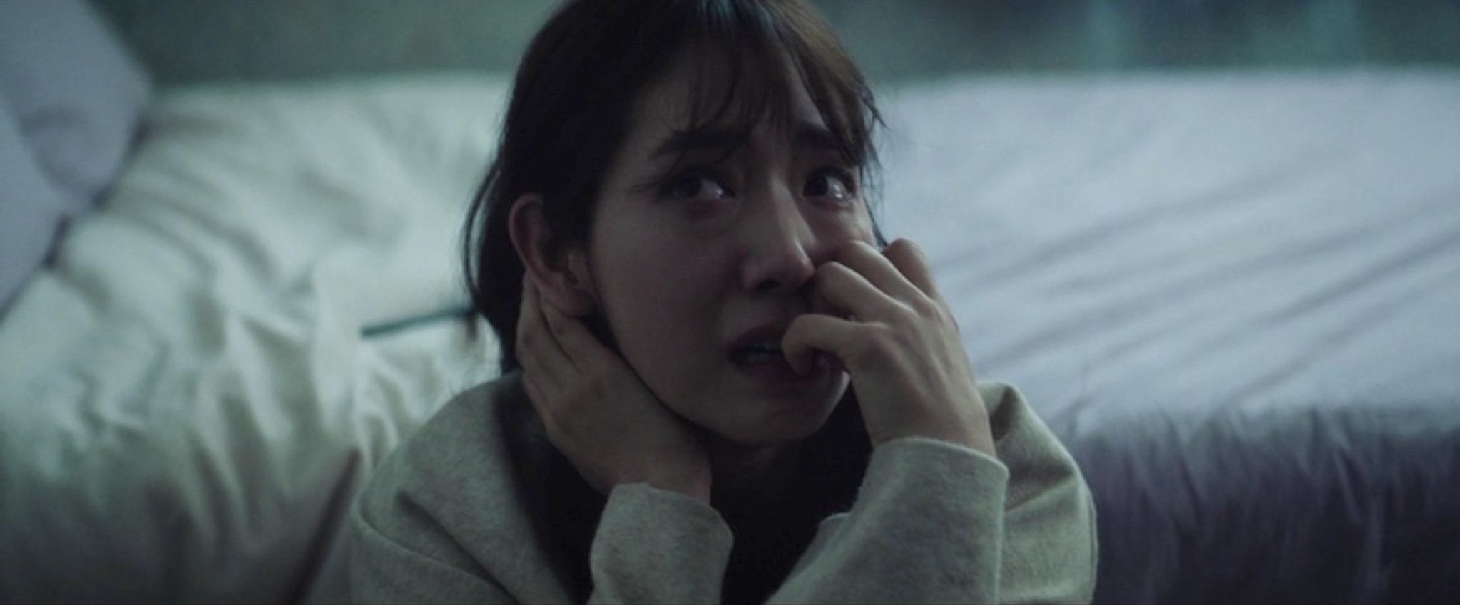 A imagem é de uma das cenas do filme. Nela, podemos ver a atriz Park Shin Hye sentada no chão, em frente à sua cama. Park é uma mulher de traços orientais, cabelos castanhos na altura dos ombros e franja. Ela veste uma blusa branca de mangas longas. Park está com uma feição assustada, com o olhar voltado para o canto superior esquerdo e roendo as unhas da mão esquerda.