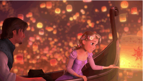 O gif mostra os personagens Flynn Rider e Rapunzel em um barco. Ela está com um vestido lilás de mangas compridas e tem seu cabelo loiro trançado com flores. Ele usa uma camisa branca e um colete azul. Ao fundo vemos centenas de luminárias de papel voando.