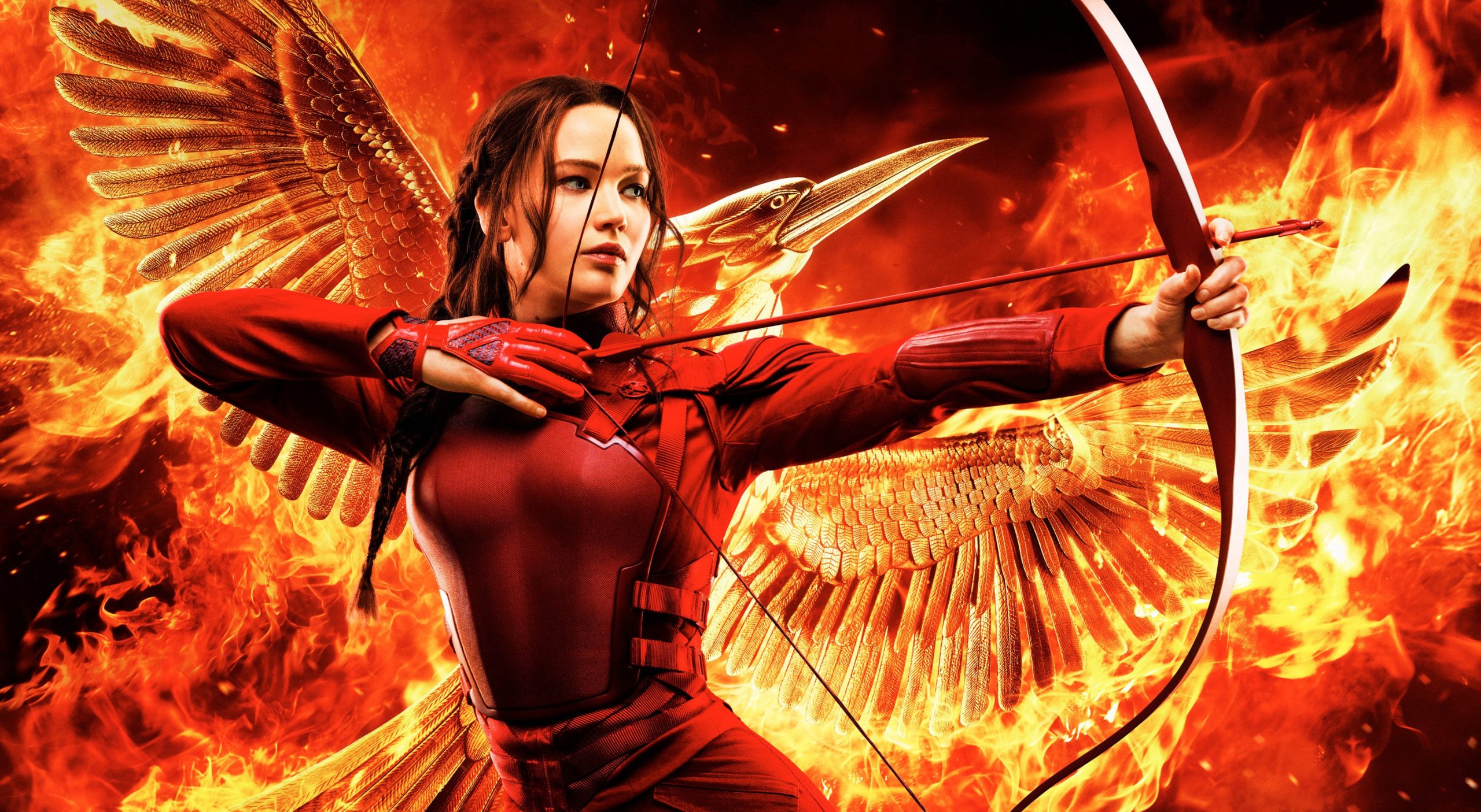 A imagem mostra Katniss com um macacão vermelho. Ela está segurando um arco e flecha pronto para ser disparado e seu cabelo, castanho escuro, está penteado em uma trança lateral. Ao fundo vemos uma ave, o tordo, em chamas.