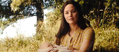 O Gif mostra Peeta brincando com uma criança loira, ambos estão com roupas brancas. Mostra também Katniss de cabelos soltos e um vestido amarelo, com um bebê no colo. Todos eles estão ao ar livre.
