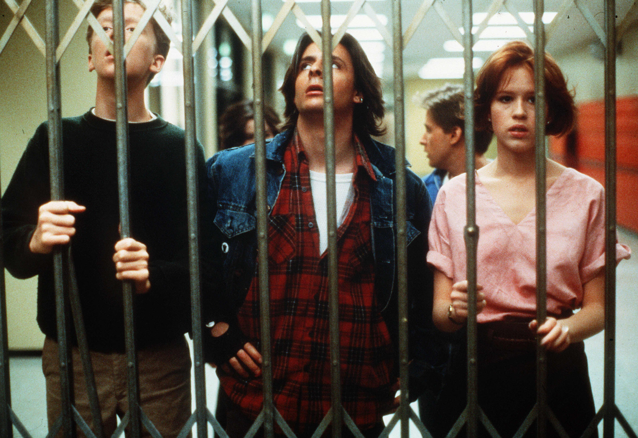A imagem é de uma das cenas do filme, em que os personagens estão atrás de um portão dentro da escola. Na imagem, podemos ver, da esquerda para a direita, os personagens: Brian, John e Claire. Atrás deles estão Allison e Andrew. 