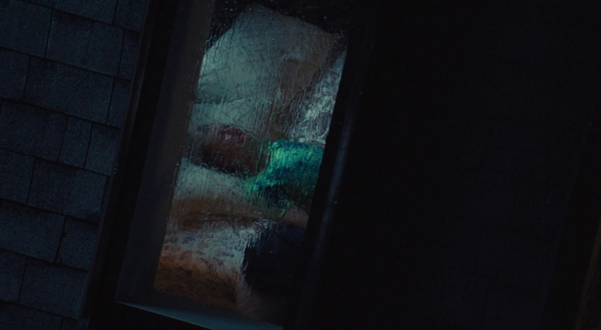 Cena do episódio Part 2: Jules de Euphoria. A cena filma a janela da casa de Jules e o vidro está embaçado e desfocado por conta da chuva. Vemos apenas o contornos da garota, sua pele clara, cabelos brancos e blusa verde. Ela está deitada na cama, chorando e olhando para o teto. 