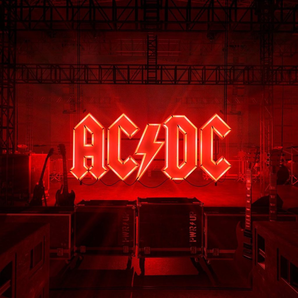 A imagem é capa do álbum Power Up da banda AC/DC. A imagem é o fundo de um palco musical, com vários instrumentos e caixas de som. No centro da imagem há o nome da banda “AC/DC” escrito como se fosse um letreiro na cor vermelha. Esse letreiro espalha luz e toda imagem é iluminada com uma luz vermelha.
