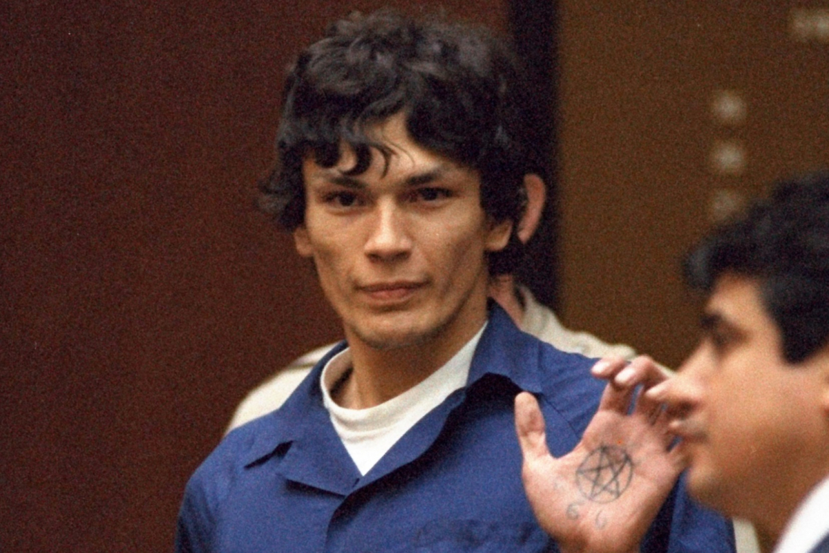 Cena da série Night Stalker: The Hunt For a Serial Killer. Na cena, vemos o assassino Richard Ramirez, um homem hispanico de pele clara e cabelos pretos, sendo levado embora de um tribunal. Ele estende a palma da mão esquerda, que mostra a tatuagem de um pentagrama.