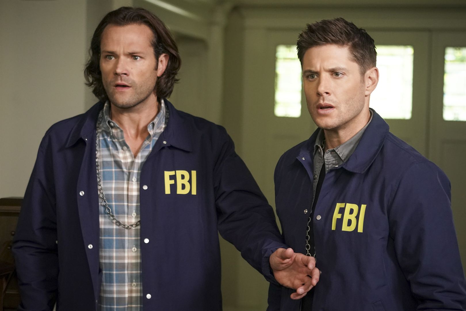 Cena de Supernatural. Sam e Dean estão vestidos com roupas do FBI, uma jaqueta azul por cima de suas roupas em um fundo claro. Eles olham espantados para algo fora da imagem e Sam está com a mão no abdômen de Dean.