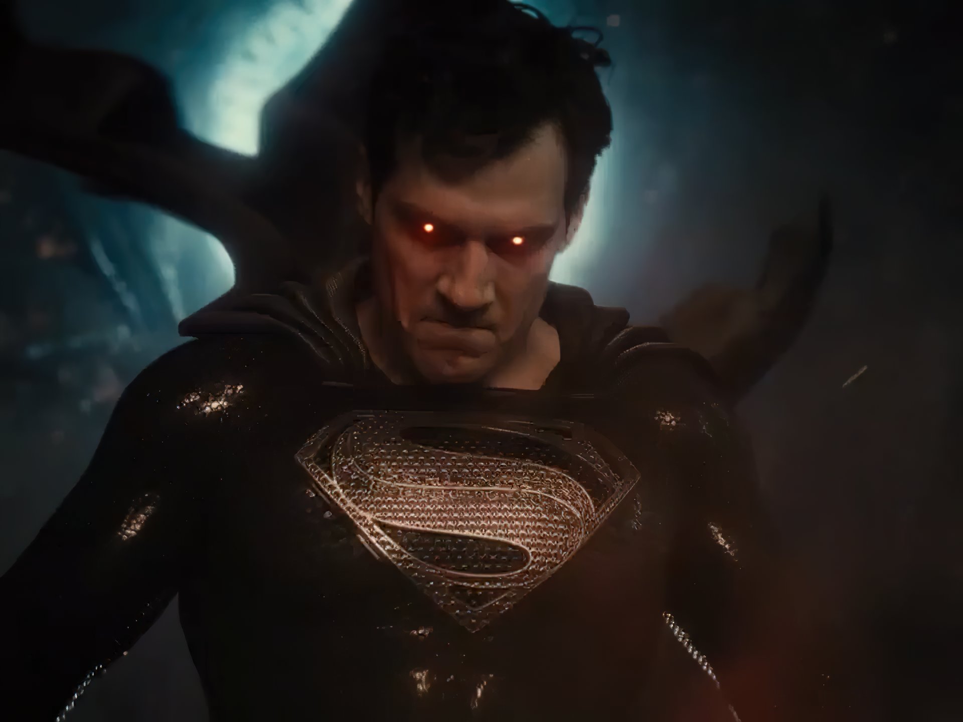 Superman (Henry Cavill) encara furiosamente a câmera, com seus olhos brilhando avermelhados, momentos antes de sua visão de calor atingir o alvo. Ele usa uma versão inteiramente preta de seu uniforme clássico, salvo pelo “S” prateado, brilhando no peito e adornado por pequenos entalhes.