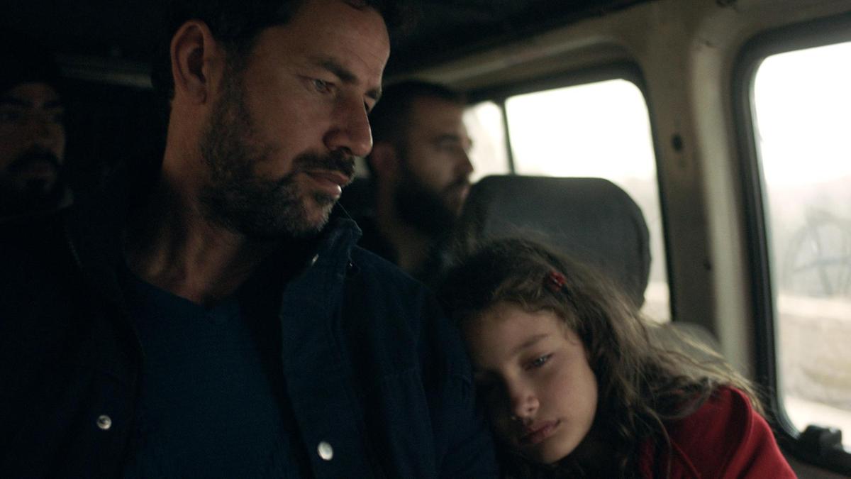 Cena do curta The Present. Nela vemos pai e filha sentados dentro de uma van. Ambos de pele clara, a filha usa um casaco vermelho e apoia a cabeça no braço do pai. 
