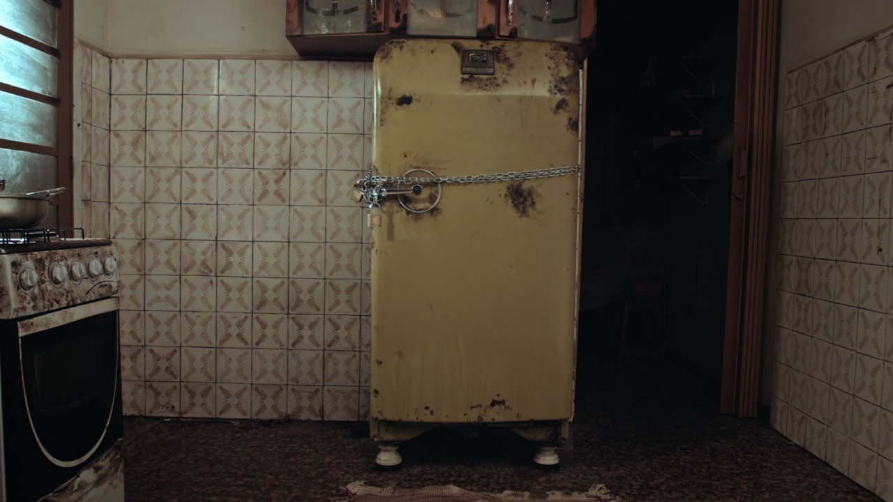 Cena do curta Nervo. Nela, vemos uma geladeira amarela trancafiada. O cenário da cozinha é de sujeira extrema.