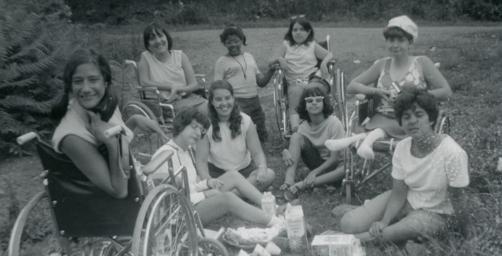Imagem em preto e branco do filme Crip Camp: Revolução pela Inclusão. A fotografia registra um grupo de jovens mulheres campistas, que posam sorridentes para a câmera em um gramado.