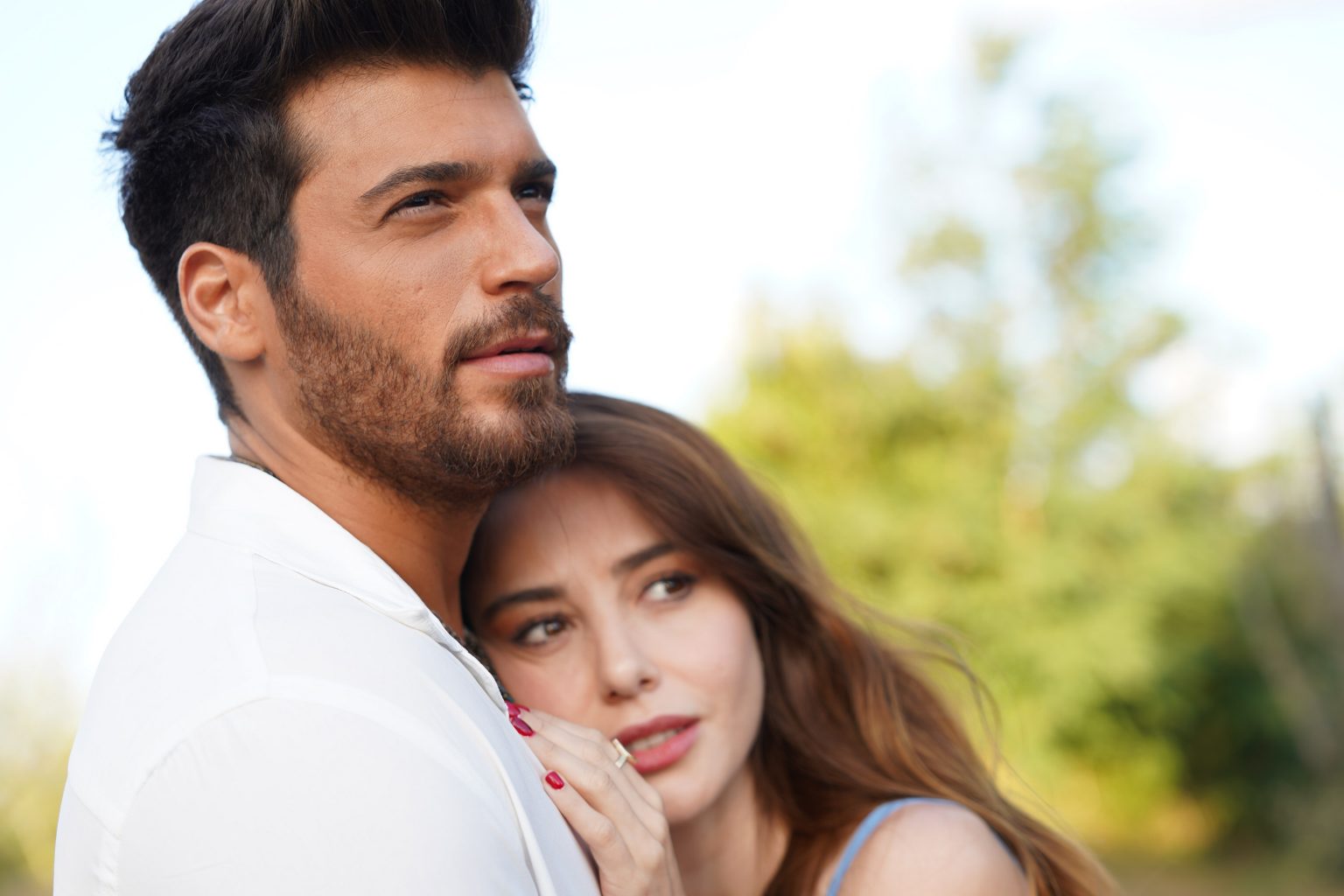 Cena da novela Bay Yanlis. Na imagem, os protagonistas estão abraçados, com Ezgi está encostada com a cabeça no peito de Özgür. Ele veste uma camisa branca e olha para a frente, enquanto a personagem feminina veste uma blusa de alças.