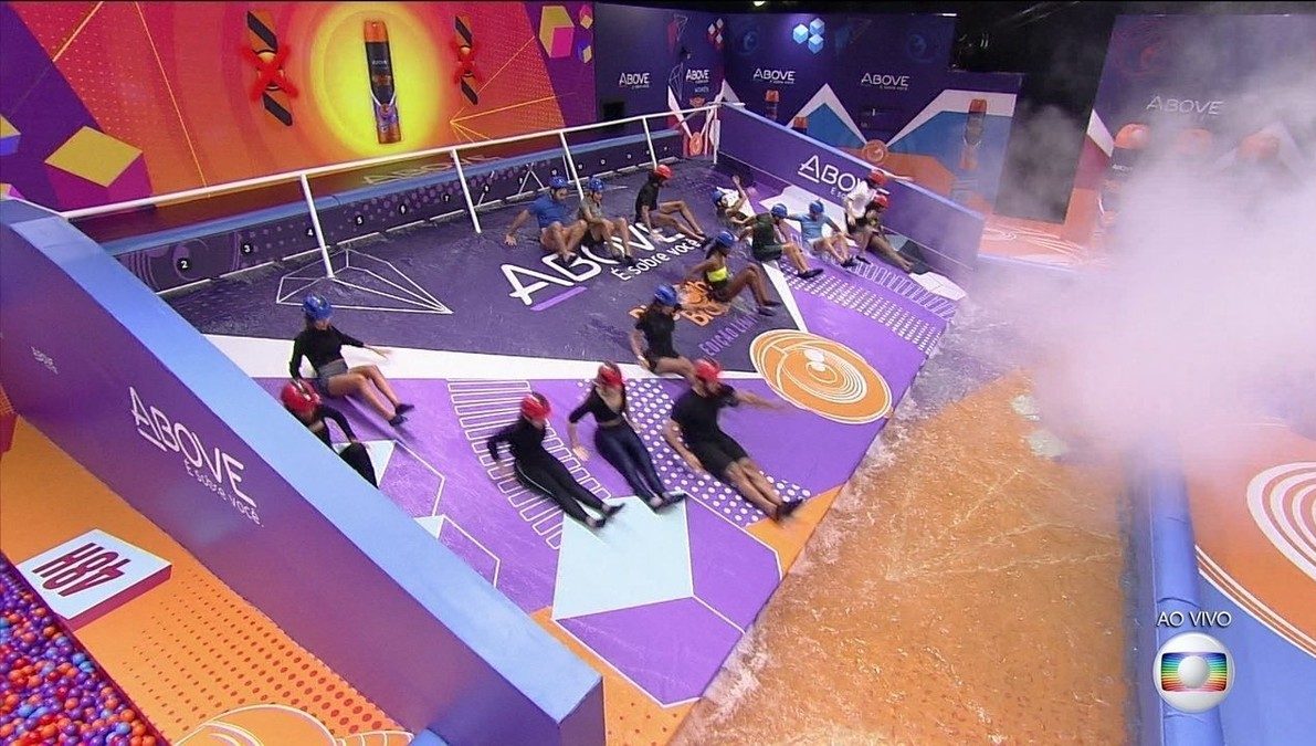 Cena do Big Brother Brasil 21. A imagem mostra os brothers que participaram da prova da Above descendo a rampa de largada em direção a uma piscina de água. Eles vestem capacetes. 