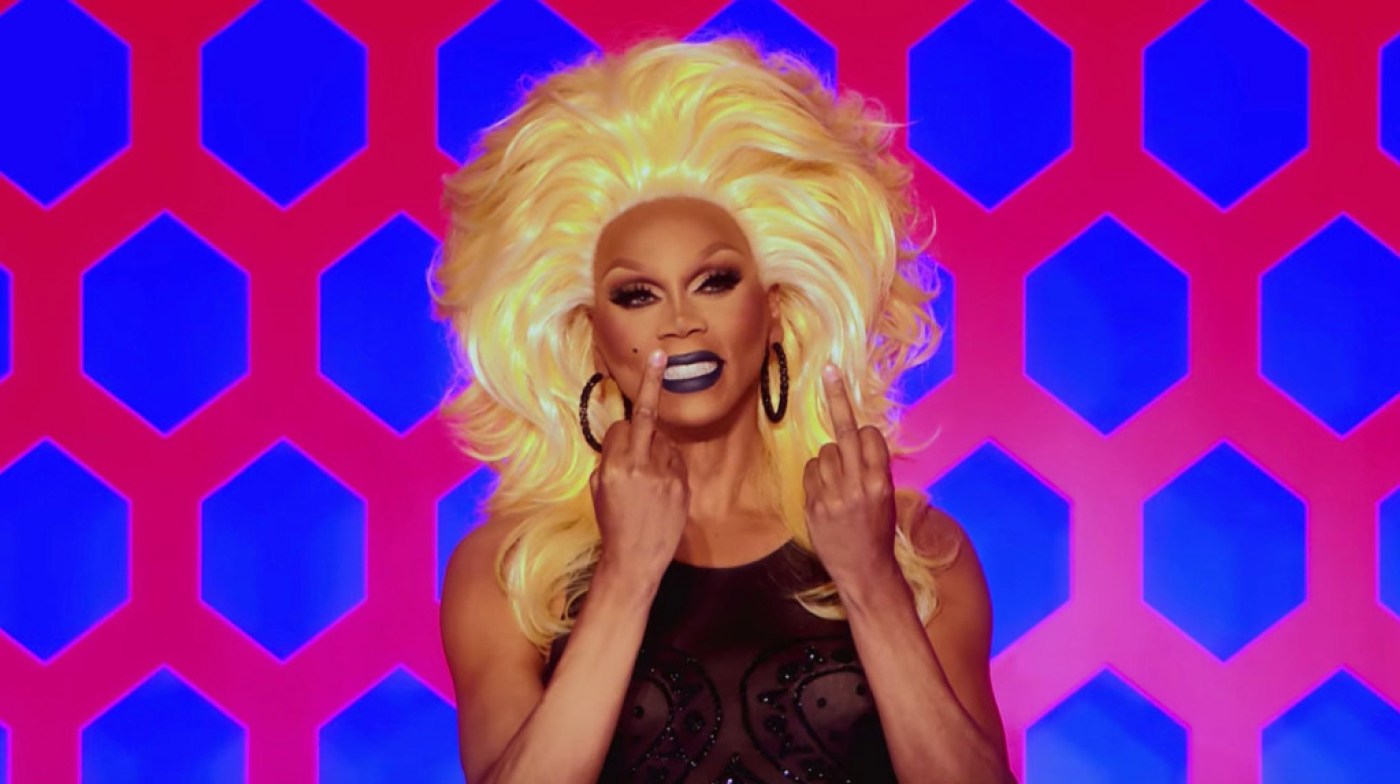  Cena da 13ª temporada do reality show RuPaul’s Drag Race. Nela, vemos RuPaul, de peruca loira e vestido preto, sorrindo enquanto levanta seus dois dedos do meio em direção à Utica. 