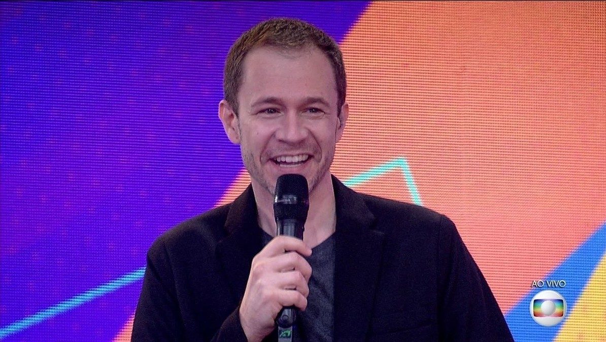 Cena do Big Brother Brasil 21. O apresentador Tiago Leifert sorri enquanto segura o microfone. 