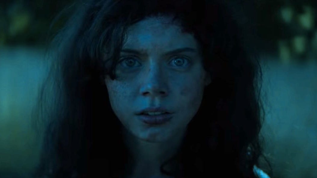 Cena do filme Rua do Medo: 1666 - Parte 3. Na cena, vemos a Sarah Fier original em close, uma mulher branca, de olhos azuis e cabelo preto. Ela tem uma expressão de medo no rosto, e a foto foi tirada de noite.
