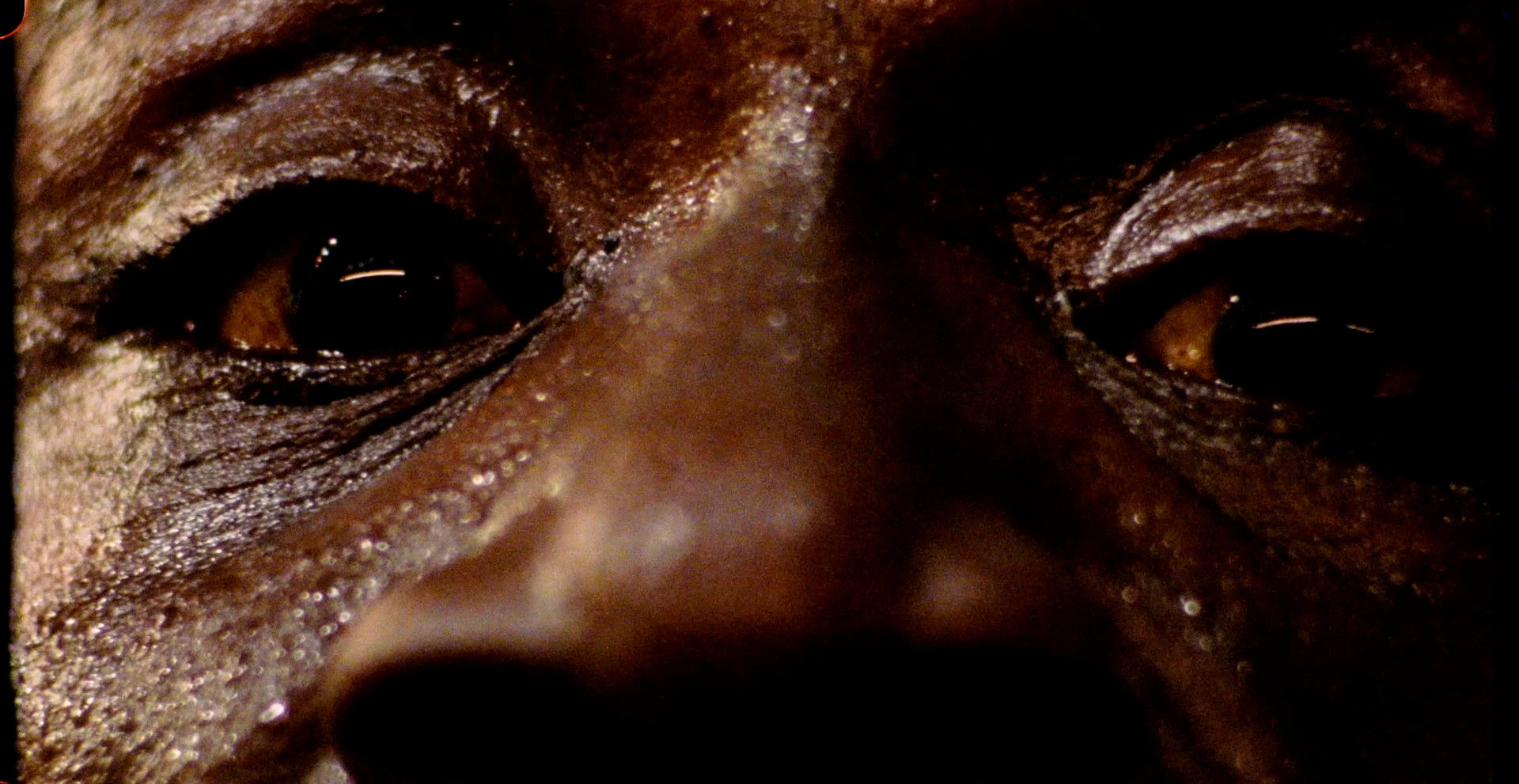Cena do filme Eu Ando Sobre a Água em que aparece um homem negro bem de perto, sendo visível apenas seus olhos e o nariz. Sua expressão é de tristeza.