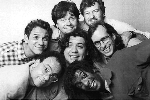 Imagem dos sete integrantes do grupo Casseta e Planeta em preto e branco. Eles estão amontoados, se abraçando e sorrindo para a câmera. 