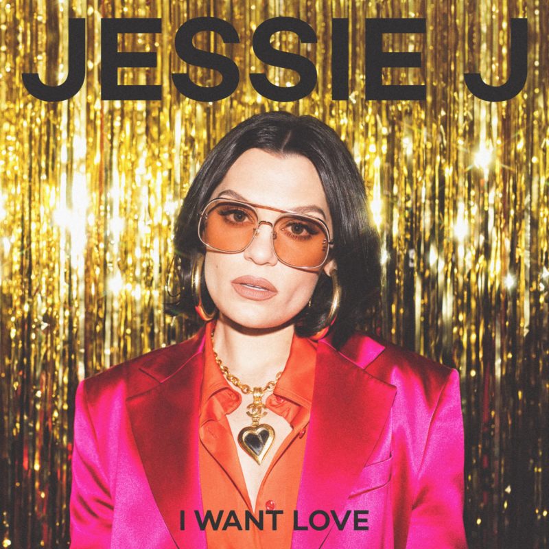 Capa do single I Want Love, de Jessie J. A cantora está num fundo dourado, usando um óculos rosa e um terno rosa. Ela usa também um cabelo preto curto chanel.