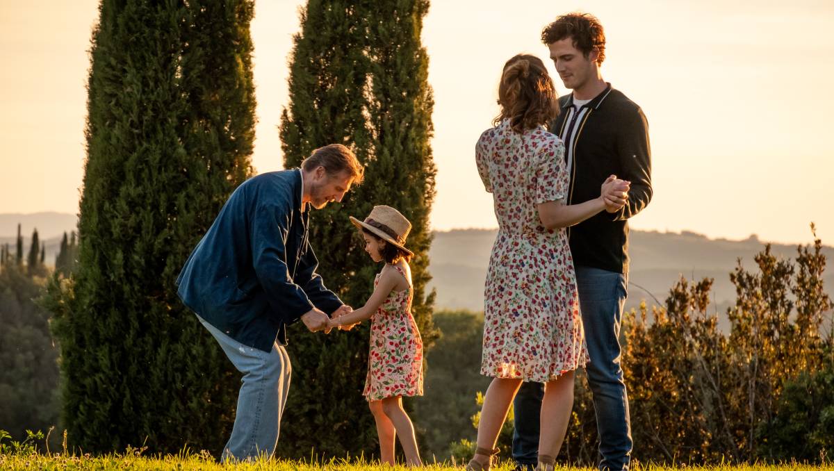 Cena do filme Made in Italy. A cena mostra 4 pessoas em um campo ensolarados: um idoso agachado com uma criança e um casal de adultos, todos brancos.