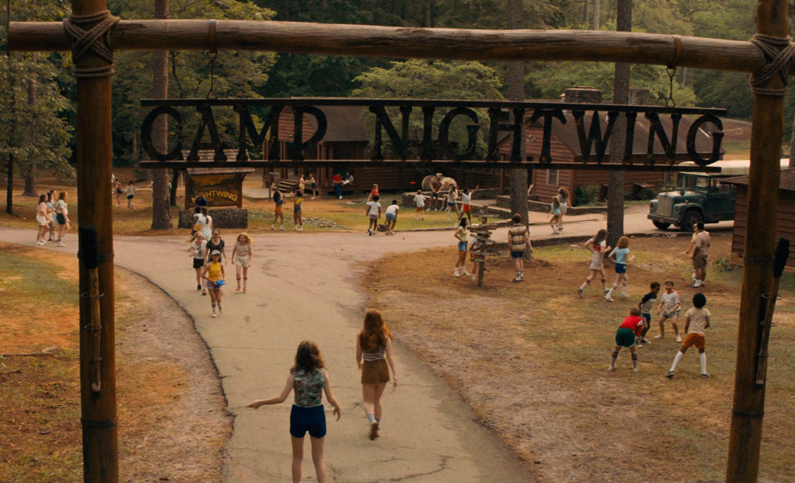 Cena do filme Rua do Medo: 1978. Podemos ver a fachada em madeira do acampamento, escrita CAMP NIGHTWING. Ela está no topo da imagem. Abaixo, vemos a entrada do acampamento, uma rua bifurcada e muitas árvores ao redor, e várias crianças andando pelo local.
