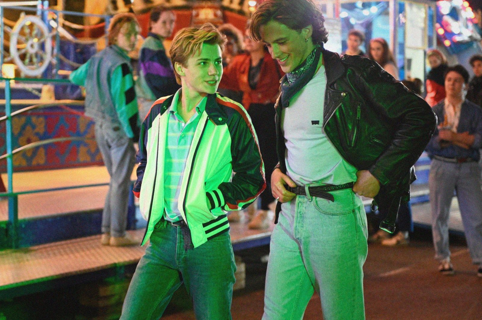 Cena do filme Verão de 85. Nela, dois adolescentes brancos andam em um parque de diversões à noite, eles se olham e sorriem um para o outro.