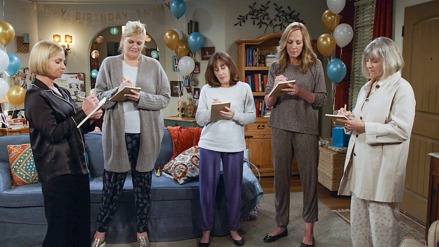 Cena da série Mom que mostra 5 mulheres em pé, usando pijamas e escrevendo em cadernos.