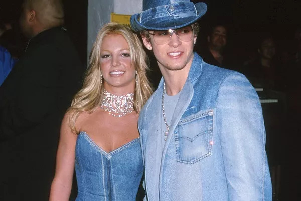 Foto de Britney Spears e Justin Timberlake. Ambos são brancos e loiros. O casal veste roupas jeans de cor azul claro. Ela usa o vestido acompanhado de um colar, e ele um terno junto de um chapéu.