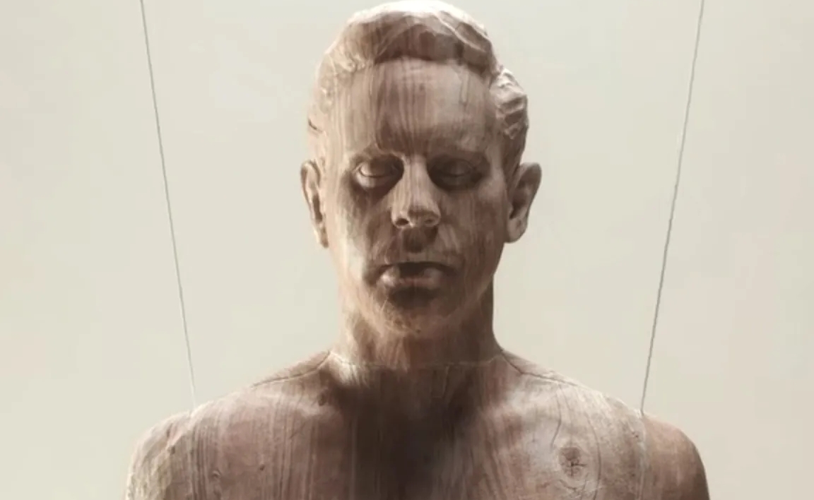 Imagem da série The Politician. Na figura há uma escultura de um busto de um homem, em madeira marrom clara. Sob um fundo branco, ainda há 2 correntes de aço segurando a escultura.