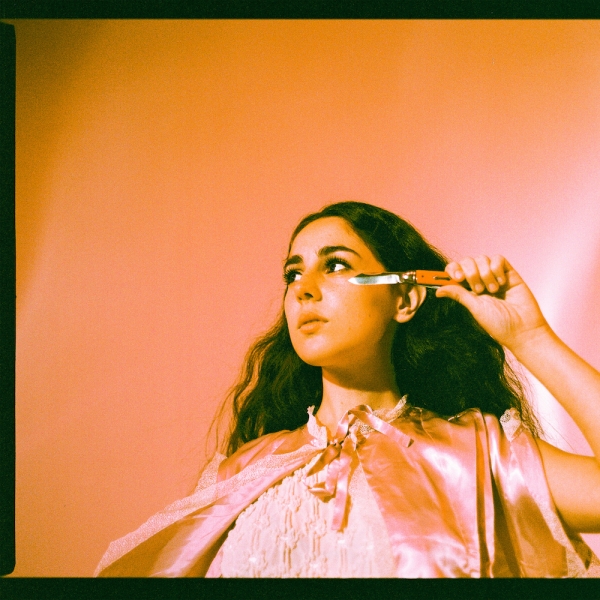 Capa do EP Scout. Na capa, à frente de uma parede laranja, a cantora Samia, uma mulher branca de cabelos castanhos longos, aparentando cerca de 20 anos e usando uma capa e uma blusa rosa clara, segura uma faca perto do próprio rosto.