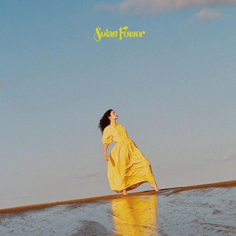 Capa do vinil do CD Solar Power, da cantora Lorde. A foto mostra Lorde, de roupa amarela, parada na praia, olhando para o céu. A foto não é reta e no topo dela, está escrito o nome do CD em fonte amarela.