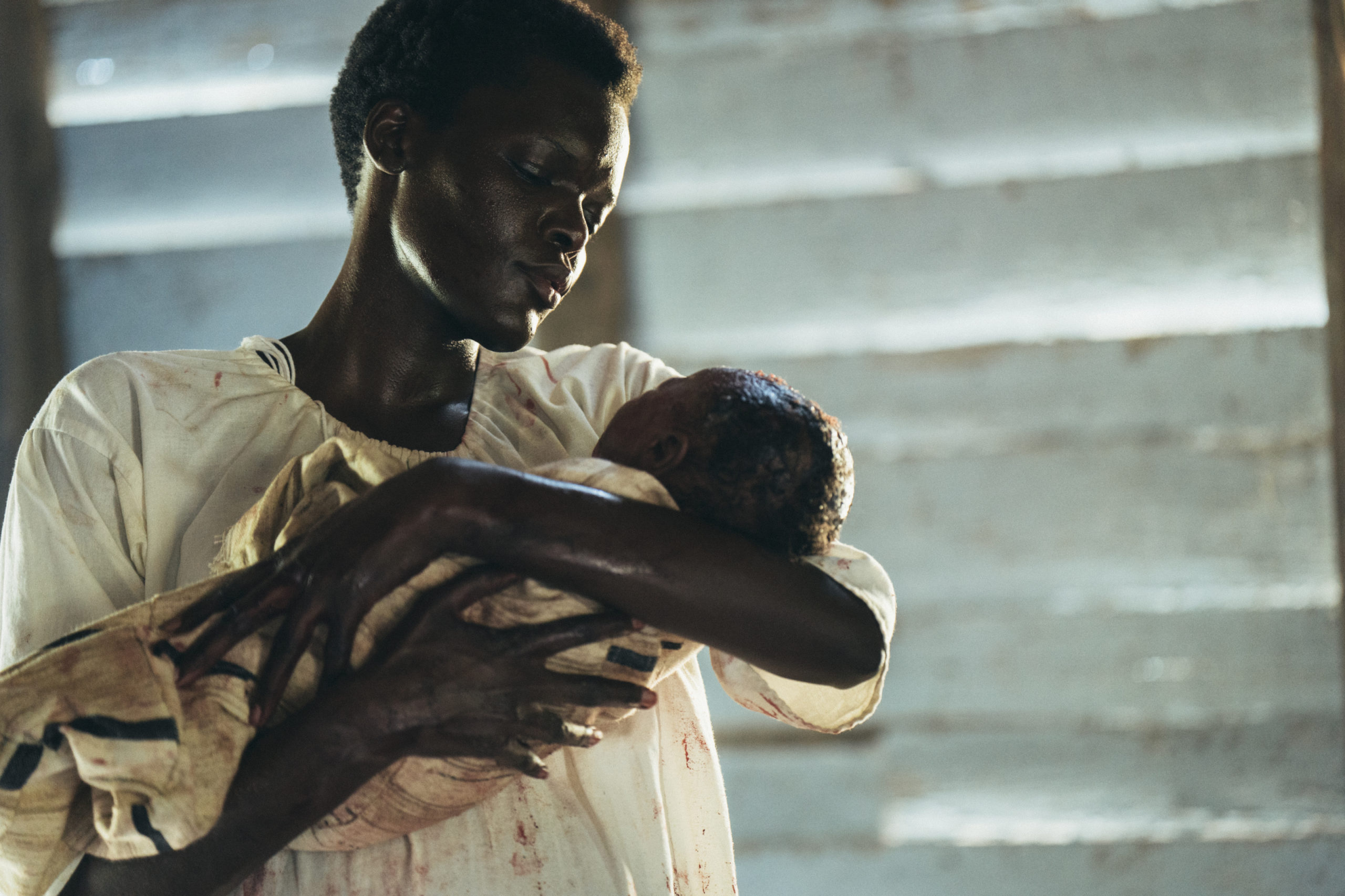 Cena da série The Underground Railroad. A cena mostra Mabel, uma mulher negra retinta adulta, vestido uma camisola branca, segurando um bebê negro no colo.