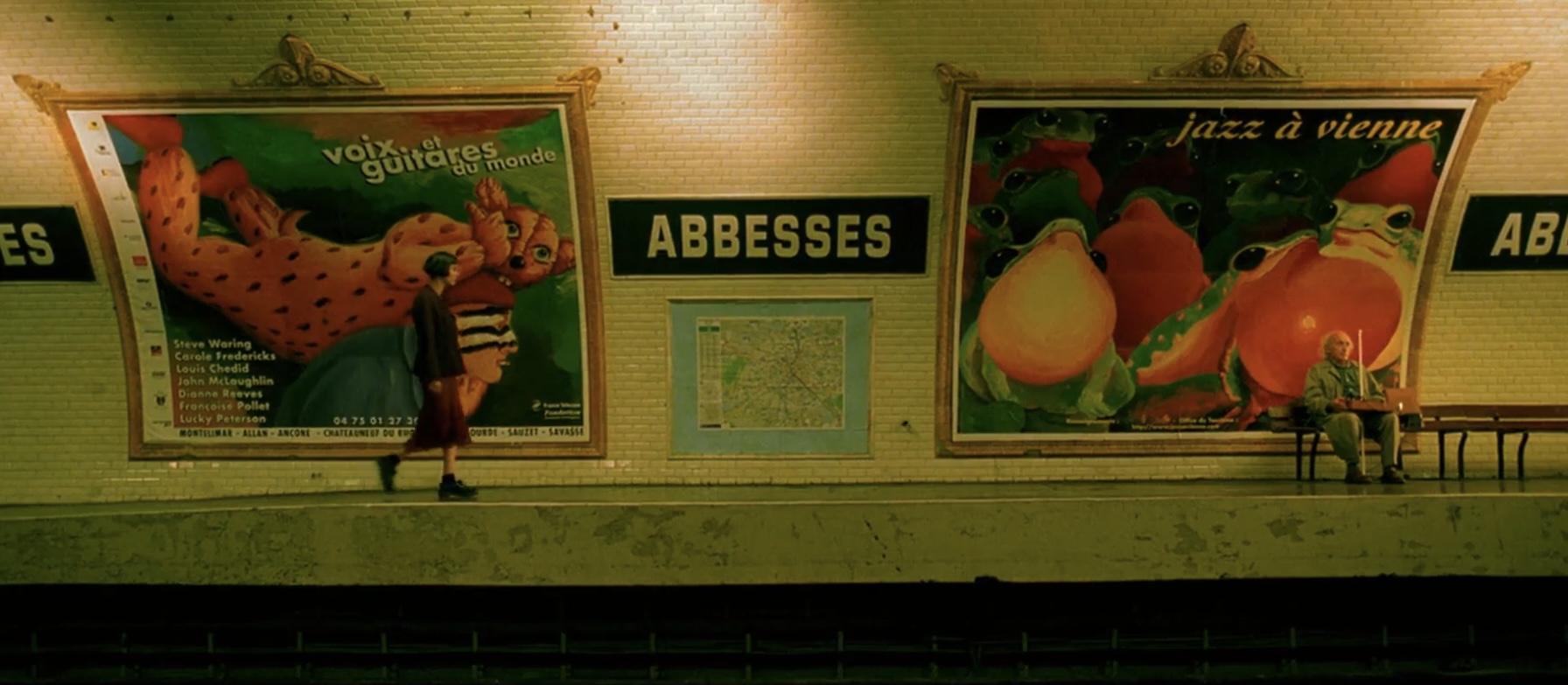 Cena do filme O Fabuloso Destino de Amélie Poulain. A imagem mostra a personagem de Amélie caminhando por uma estação de metrô, vista de longe e de perfil. A câmera está nos trilhos, capturando as paredes da área de embarque, que é preenchida por anúncios coloridos do lado esquerdo e direito, e no centro existe uma placa escrito "ABESSES". Amélie está do lado esquerdo, usando um vestido vermelho e botas pretas.