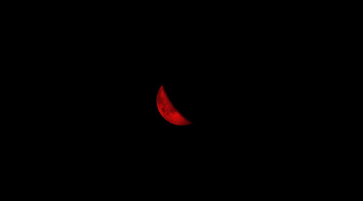 Imagem do documentário Meia lua Falciforme. No centro da imagem está apenas uma meia lua crescente colorida em vermelho e todo o fundo é preto.