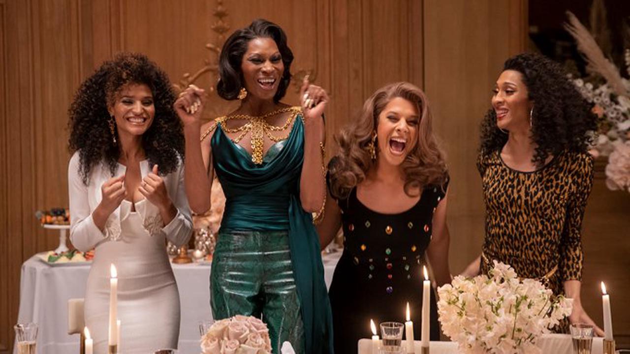 Cena da série Pose. A cena mostra 4 mulheres negras, em pé e sorrindo, uma ao lado da outra, usando roupas chiques. Á direita, está Angel, de vestido branco; Elektra, de roupa verde; Lulu, de roupa preta; e Blanca, usando vestido com estampa de oncinha.