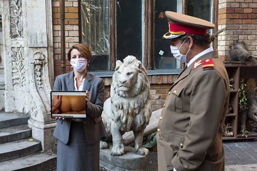 Cena do filme Má Sorte no Sexo, mostra uma mulher segurando um tablet deitado e um homem com roupa militar assistindo a tela.