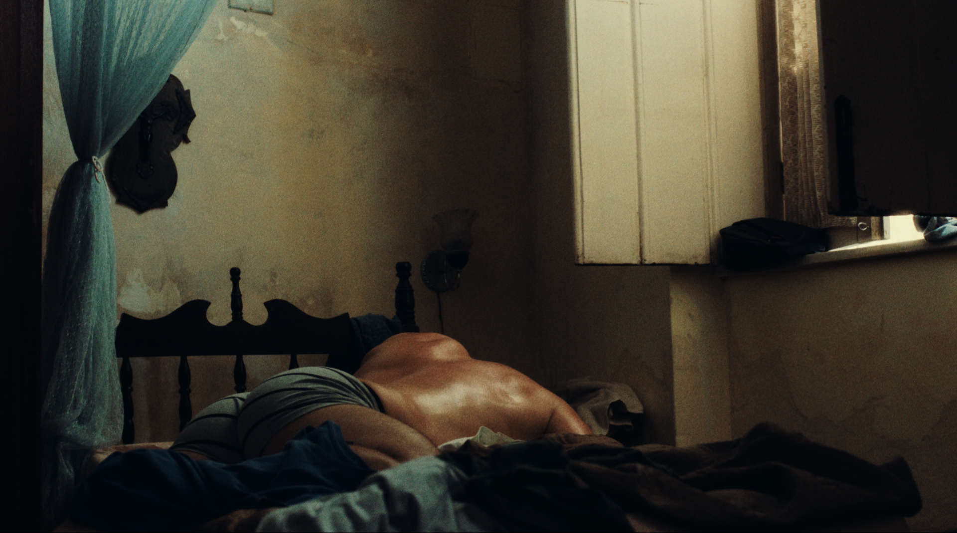 Cena do filme Deserto Particular, mostra um homem adulto de cueca deitado de bruços na cama.