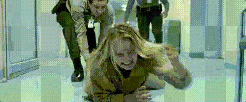 Cena do filme O Homem Invisível. Cecília (Elisabeth Moss), de cabelos loiros, usando um macacão, rasteja no chão tentando fugir de seu ex-marido enquanto dois policiais tentam segurá-la.