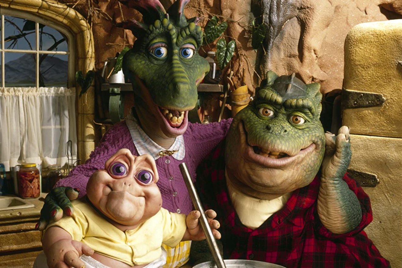 Cena da série A Família Dinossauros em que há três dinossauros reunidos na cozinha sorrindo para a foto. Os dois adultos são verdes e o bebê é rosa.