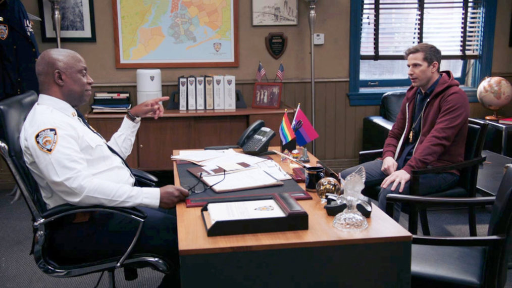 Cena da oitava temporada de Brooklyn Nine-Nine. A cena mostra o interior da sala do comandante Holt, sentado à mesa, que é um homem negro, idoso e usa camisa social branca. Do outro lado da mesa, está Jake Peralta, homem branco adulto que usa uma blusa vinho. 