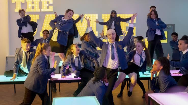 Cena de Todos Estão Falando sobre Jamie mostra um grupo de jovens performando de uniforme escolar em uma sala de aula.