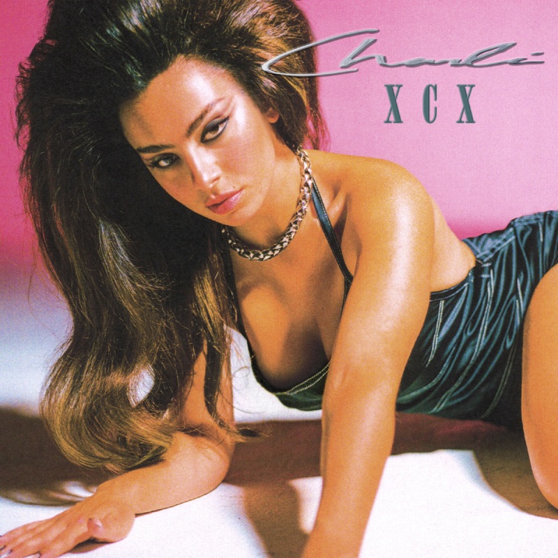 Capa do single Good Ones, de Charli XCX. A cantora está deitada apoiada no chão, com um cabelo volumoso liso. Ela é branca, usa um vestido de cetim preto e um colar prateado. O fundo é rosa. Ela está olhando para a câmera, e usa maquiagem com delineado. 