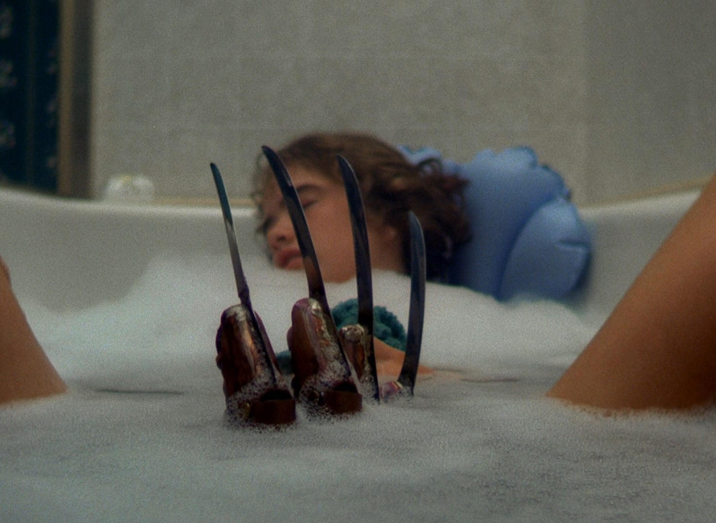 Cena do filme A Hora do Pesadelo. A imagem mostra a personagem Nancy, interpretada pela atriz Amanda Wyss, numa banheira de banho. Ela é uma jovem branca, loira, de cabelos curtos, e está apoada nas costas da banheira, de olhos fechados e com as pernas abertas. No meio, surge a luva de tesouras de Freddy Krueger,