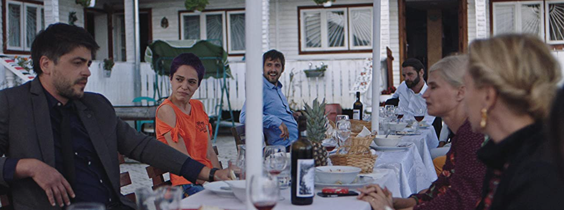 Cena do filme Lua Azul mostra uma família fazendo uma refeição em volta de uma mesa branca e farta.