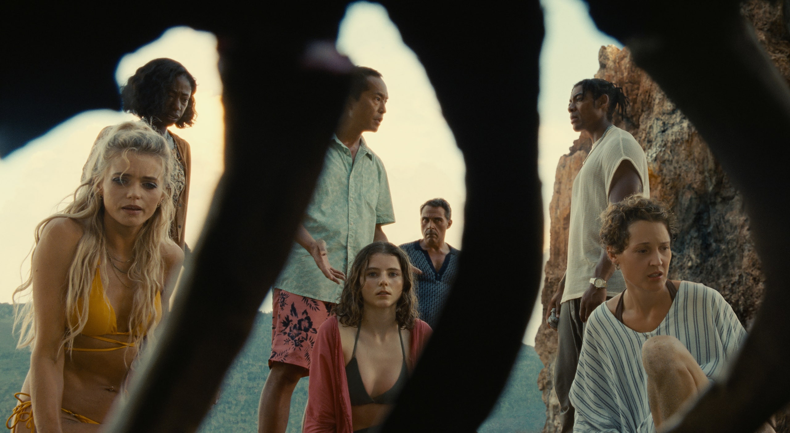 Cena do filme Tempo exibe sete pessoas numa praia, quatro mulheres e três homens. As mulheres observam a ossada de um ser humano, enquanto dois homens discutem e o outro observa, ao fundo.