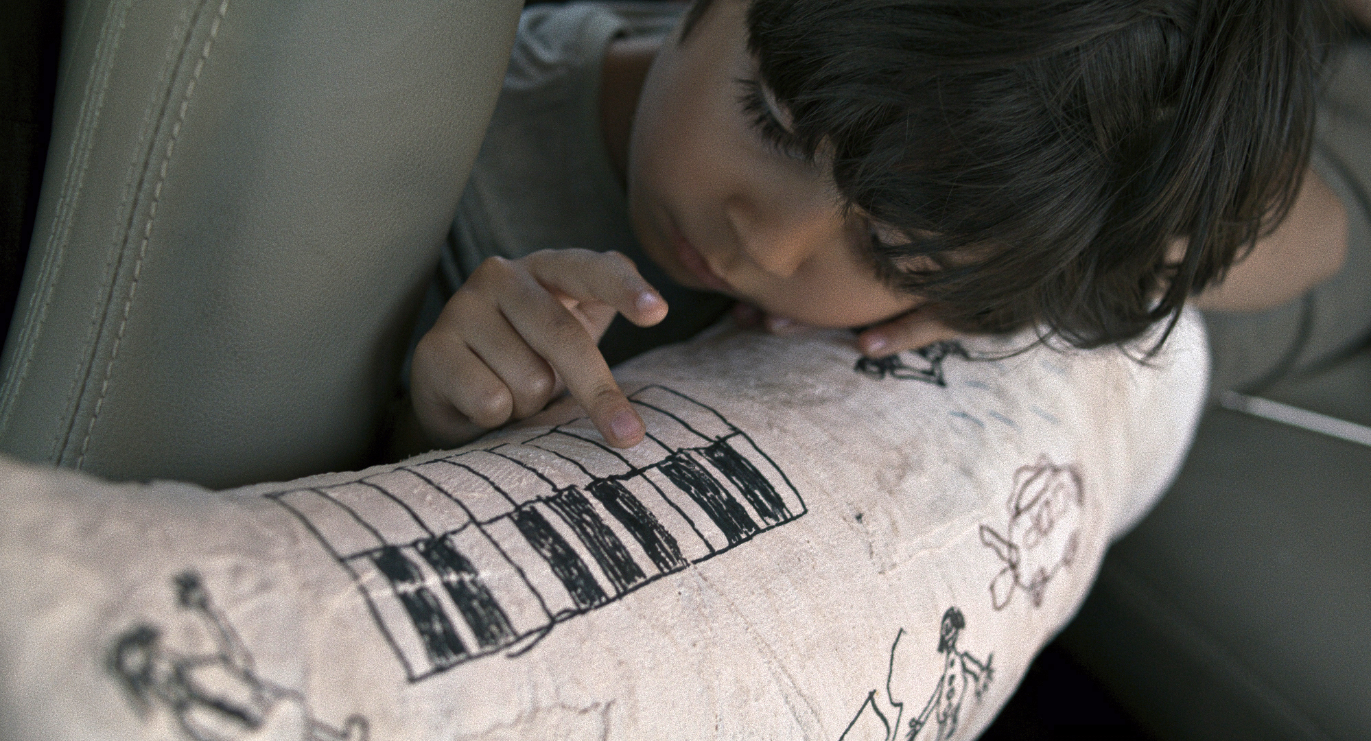 Cena do filme Pegando a Estrada. A foto mostra de perto um menino pequeno apoiado sobre uma perna engessada, na qual se vêem alguns desenhos. Ele apoia seus dedos sobre a imagem de teclas de um piano.