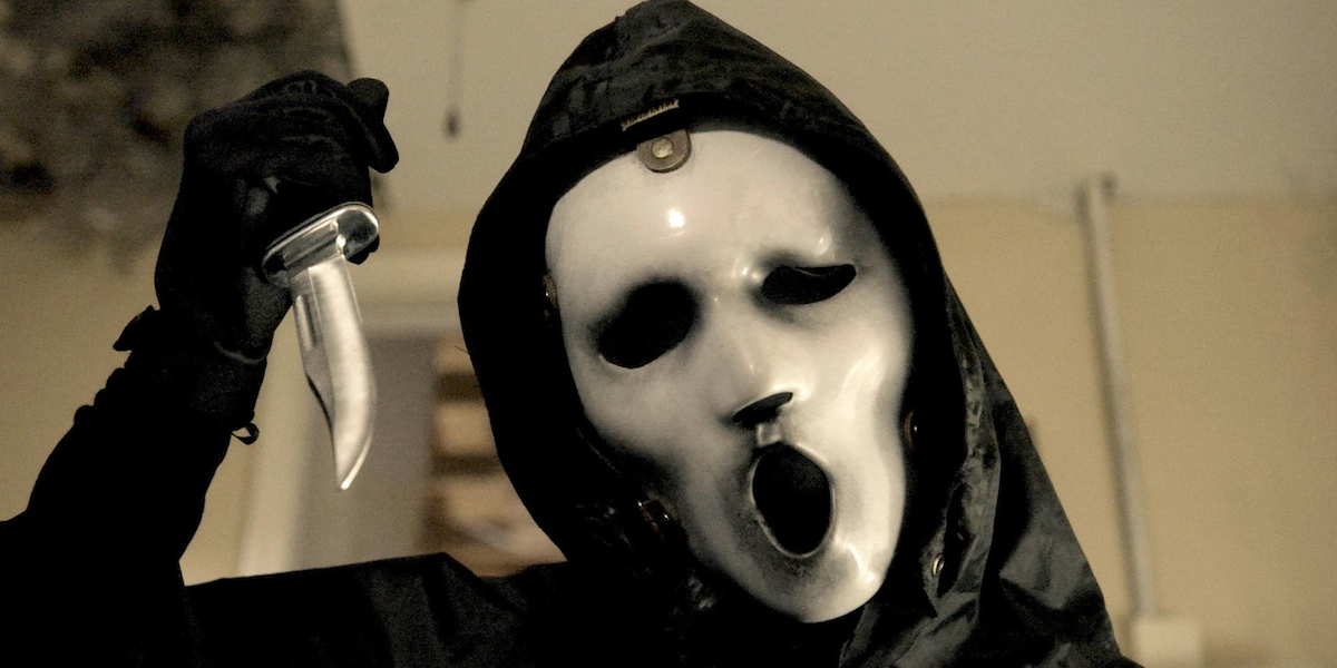 Cena da série Scream. Na foto, em um primeiro plano, vemos uma pessoa vestindo uma capa preta, luvas pretas e uma máscara cirúrgica branca, empunhando uma faca.