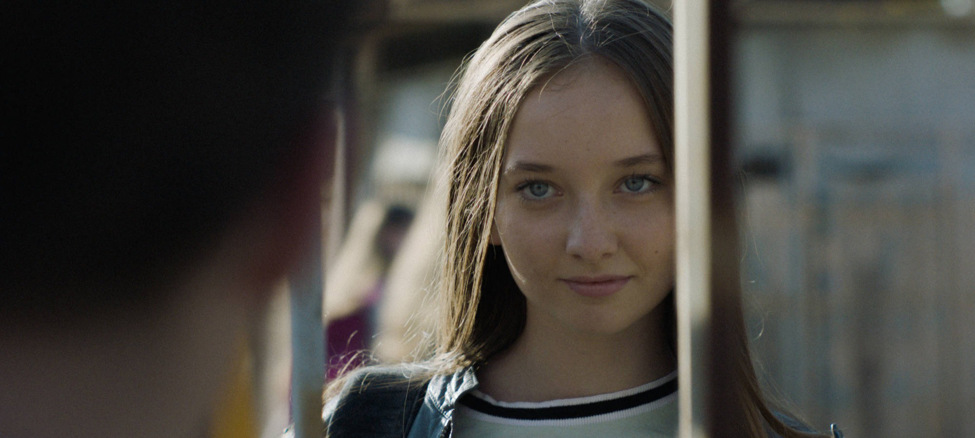 Cena do filme Irmandade, mostra uma garota branca e jovem de olhos claros e cabelos compridos olhando para a frente.