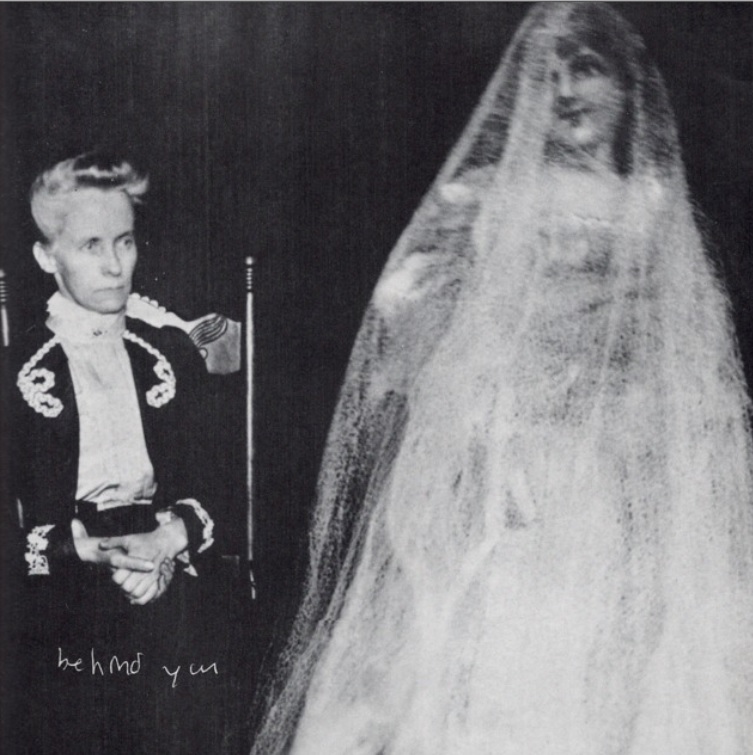 Imagem do livreto encontrada na página 81. Uma foto em preto e branco na qual na esquerda está um homem sentado com os dizeres "Behind you" na parte inferior esquerda da imagem. Na parta direita da imagem está o fantasma de uma mulher vestida de noiva.